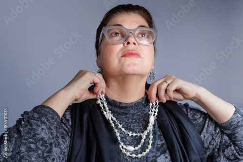 Woman wearing glasses adjusting a layered pearl necklace while looking upward.