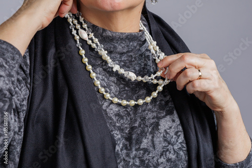 Close-up of hands adjusting a layered pearl necklace against a textured outfit.