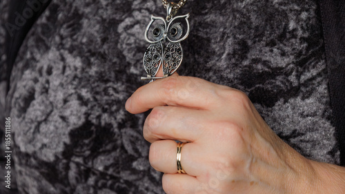 Close-up of a hand holding an owl pendant necklace against textured fabric.