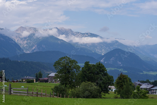 Scenic mountain countryside with open meadows, forested slopes and small rural homes. Calm natural environment, fresh air, travel destination and outdoor lifestyle concept.