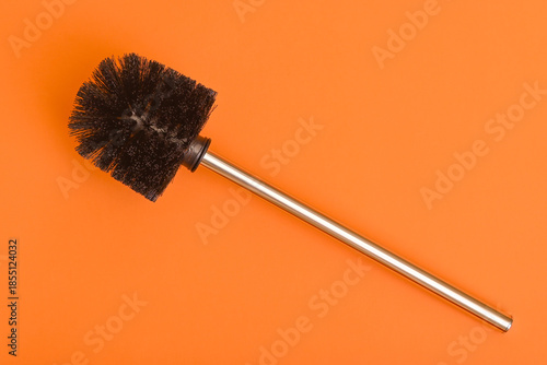 Toilet brush with metal handle on orange background