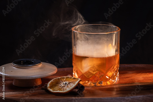 Smoked whiskey cocktail served on the rocks with dramatic lighting served on a wooden surface.