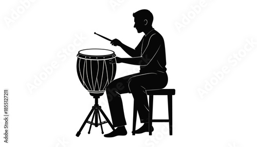 Silhouette of a man playing a conga drum on a stool.