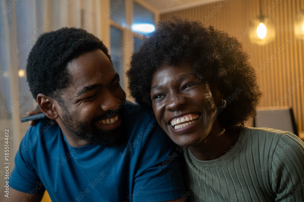 Obraz premium Happy laughing Black couple bonding while relaxing sitting on sofa