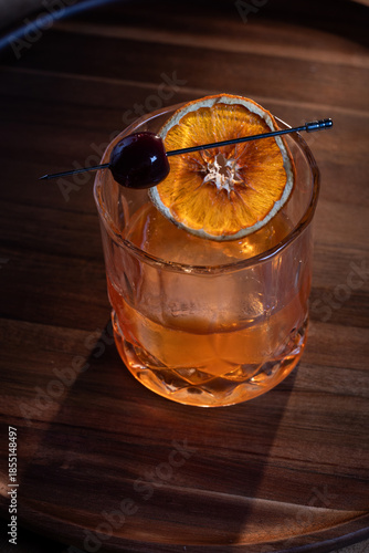 whiskey cocktail served on the rocks garnished with a dehydrated orange slice with dramatic lighting served on a wooden surface.