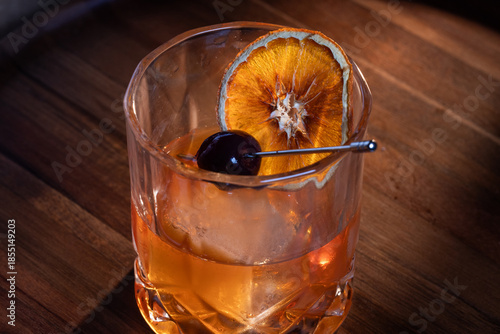 Beautiful garnish of a dehydrated orange slice and a dark cherry on a whiskey cocktail served on the rocks.
