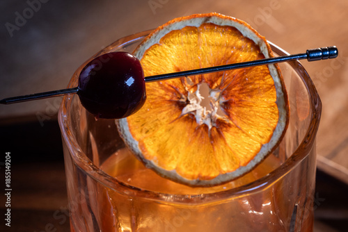 Beautiful garnish of a dehydrated orange slice and a dark cherry on a whiskey cocktail served on the rocks.