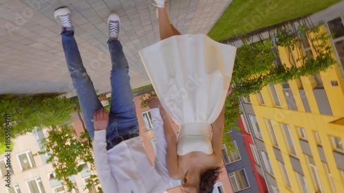 Young couple, smiling bride in a white gown and groom stroll through a modern residential courtyard with colorful buildings, holding hands 4K UHD B-Roll footage