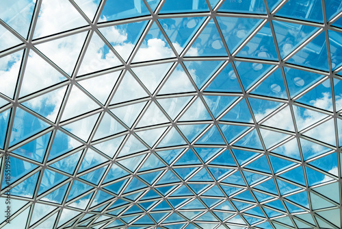 Fotografie Glass ceiling with geometric pattern reflecting a vibrant blue sky and scattered clouds