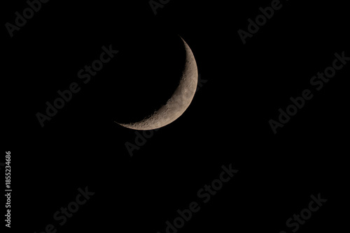 Thin crescent moon against deep black night sky. Minimalistic astronomical scene with copy space, calm atmosphere and clear lunar surface details.