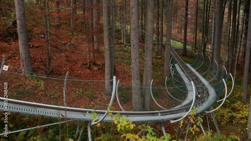 A sports slide, an amusement park, and a descent in the forest in the mountains. Dense trees with orange autumn leaves.