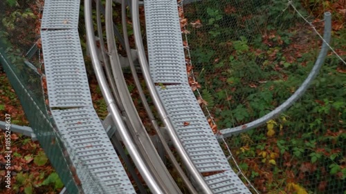 A sports slide, an amusement park, and a descent in the forest in the mountains. Dense trees with orange autumn leaves.