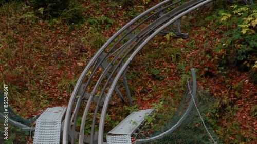 A sports slide, an amusement park, and a descent in the forest in the mountains. Dense trees with orange autumn leaves.