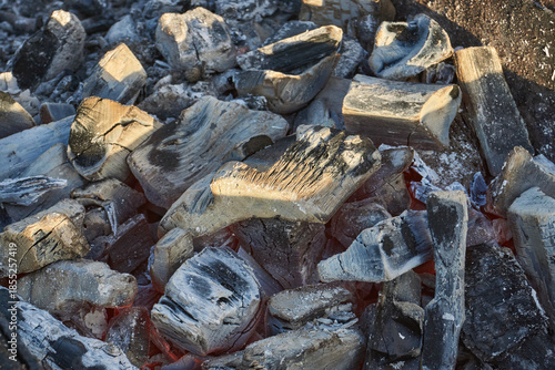 Smoldering logs and bright flames in a metal barbecue grill. Detailed close-up of fire, heat, and smoke outdoors. Flaming logs with heat and smoke rising from an open grill.