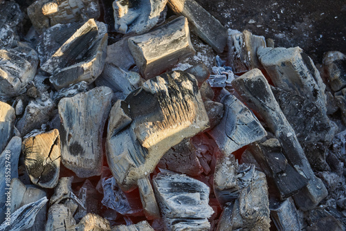 Smoldering logs and bright flames in a metal barbecue grill. Detailed close-up of fire, heat, and smoke outdoors. Flaming logs with heat and smoke rising from an open grill.
