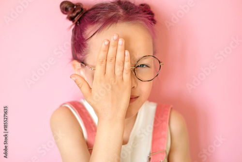 Canvas Print A child with glasses squints and tries to concentrate his vision with left eye, covering his right hand