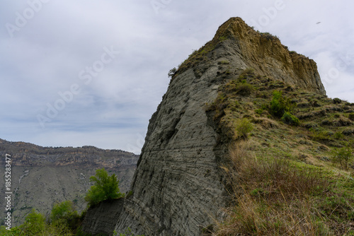 Layered rock formation with vegetation under a cloudy sky