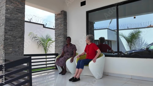 Lilongwe Malawi Africa, 01.12.2025. Video. African female  carer sitting on a patio working with an elderly Dementia sufferer  on holiday in Malawi Africa.