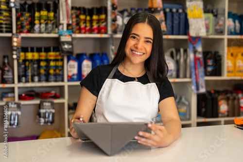 Obraz na plátne Young woman smiling while holding a tablet in a small business hardware store