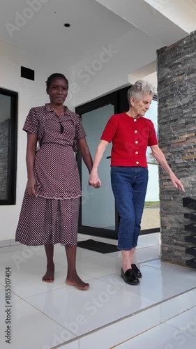 Lilongwe Malawi Africa, 01.12.2025. Video. African female  carer bare footed going for a walk with an elderly Dementia sufferer  on holiday in Malawi Africa.