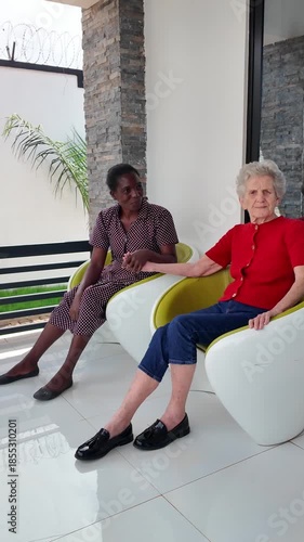 Lilongwe Malawi Africa, 01.12.2025. Video. African female  carer sitting on a patio working with an elderly Dementia sufferer  on holiday in Malawi Africa.