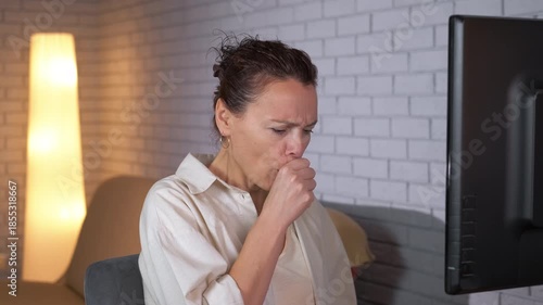 Sick woman coughing during video call with doctor. Ill woman with sore throat and fever talking with a doctor during a video call consultation, receiving professional medical advice