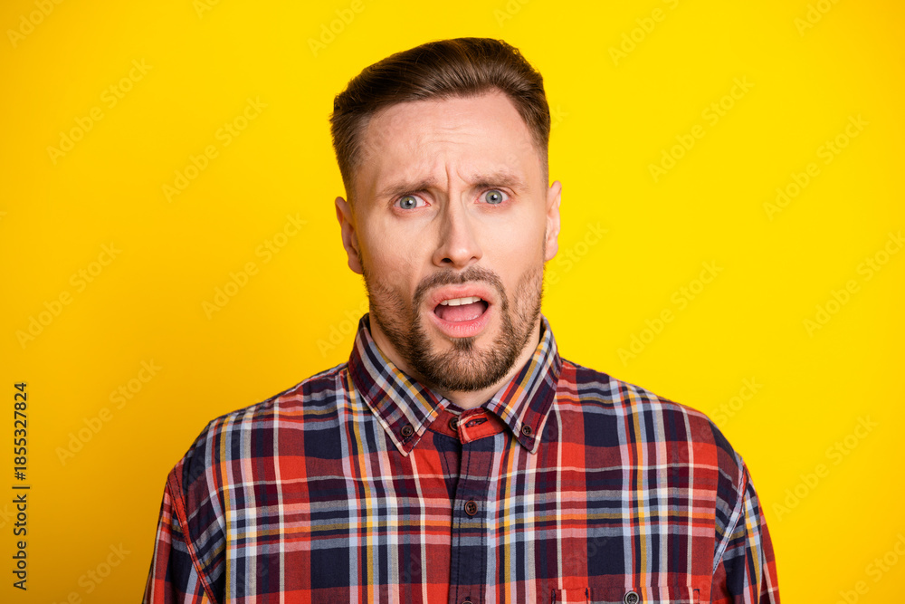 Fototapeta premium Surprised tall handsome man with plaid shirt standing against bright yellow background