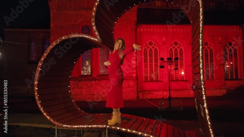 Trendy woman clad in crimson attire immersed in lively holiday illumination and bustling city atmosphere slow motion