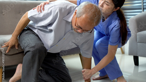 Professional Asian female nurse or caregiver helping elderly man stand up from floor at home. Young medical staff supporting senior patient suffering from pain or fall accident concept.
