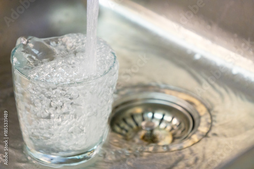 Glass Filling With Fresh Water.Clear glass being filled with fresh tap water in a stainless steel sink, symbolizing cleanliness, hydration, domestic routine, and safe drinking water concept.