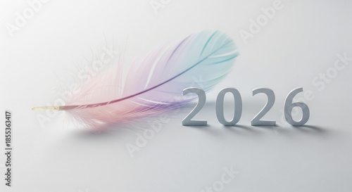 A pastel colored feather with a metallic sheen lies next to 2026 gray metallic numbers on white background