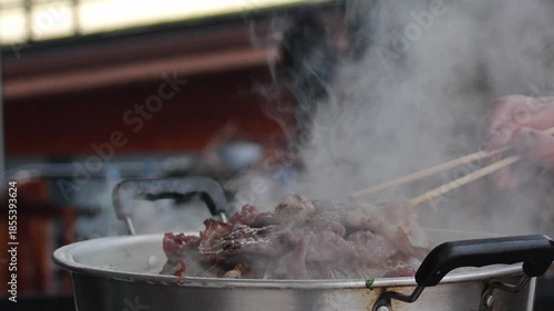 4K Close-up of meat grilling on hot barbecue pan with rising steam and chopsticks turning the food, Concept of Asian cuisine comfort food street food culture.