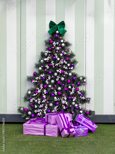 Decorated Christmas tree with purple ornaments and pile of presents beneath in room interior