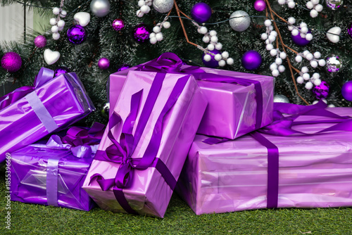 Pile of wrapped gifts next to a Christmas tree inside modern interior