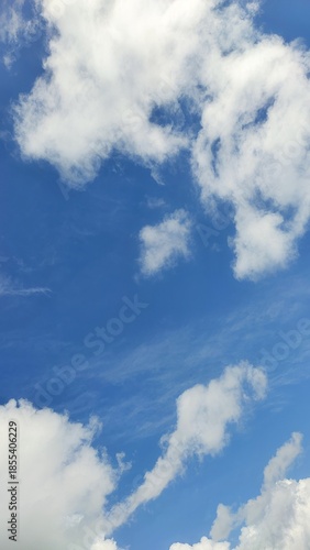 Vertical view of bright blue sky with fluffy white cumulus clouds and wispy natural atmospheric textures.