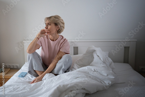 Foto Sleepy tired middle aged woman with exhausted expression woke up in morning after restless night, sitting and yawning in bed in bedroom, bored and lazy, seasonal insomnia, strength loss issues
