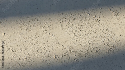 Sunlit textured wall surface with strong diagonal shadows highlighting its rough and uneven characteristics, creating an interesting play of light and shade for background aesthetics