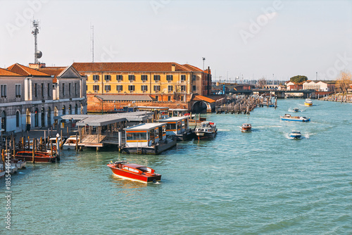 Water transport hub at Piazzale Roma in Venice, Italy, showing various public vaporetto and private water taxis navigating of Grand Canal. Traditional Venetian architecture and modern bus terminal
