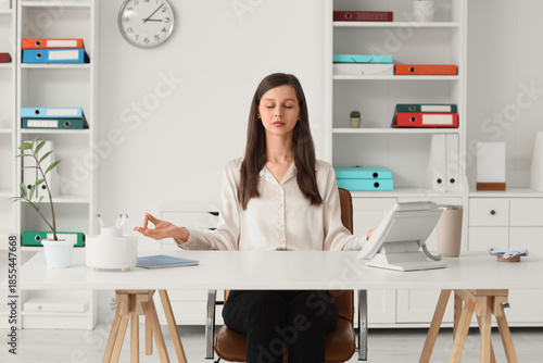 Young businesswoman meditating at table in office