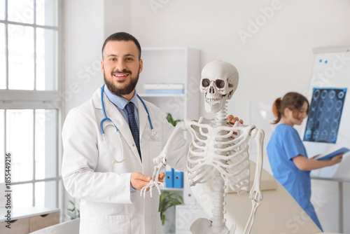 Male doctor examining arm bone of human skeleton model in clinic