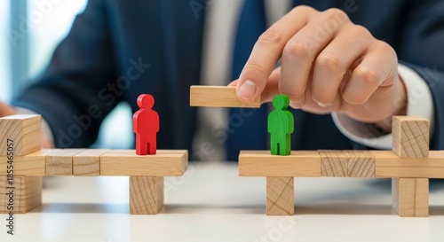 Hand builds wooden bridge between two figurines. Mediator solving conflict. Bridge represents understanding and connection. Figures symbolize people groups. Mediation and conflict resolution concept.