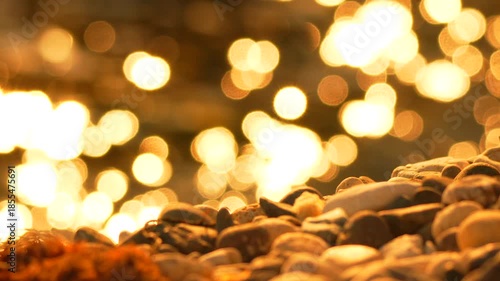Pebbles bokeh sunset reflection close up shot of golden light dancing on water surface at the beach.