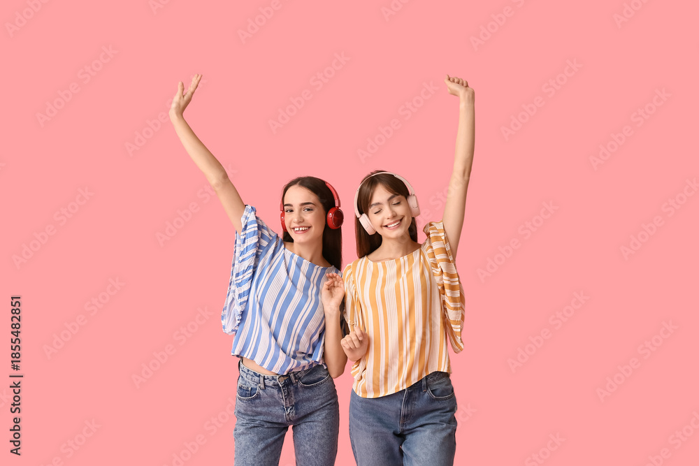 Fototapeta premium Beautiful young twin sisters in modern headphones on pink background