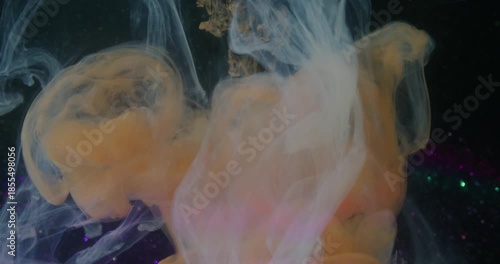 Paint drop. Swirling mist. Defocused orange blue purple color glitter broken light bulb floating on abstract dark black background.