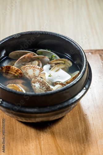 A black bowl filled with clam soup featuring fresh clams and tofu in clear broth.