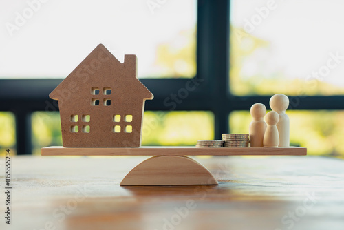 Financial balance and family home concept with wooden house, coins, and people on scale. Symbol of housing cost, income balance, family finance, real estate investment, and economic stability.
