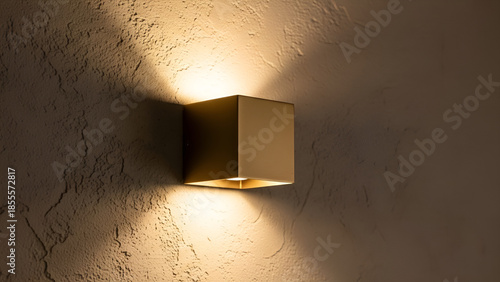 Modern golden cube-shaped outdoor wall lamp casting warm light onto a textured wall
