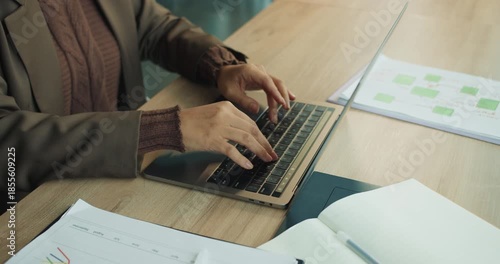 Desk scene showing hands typing with documents and graphs present