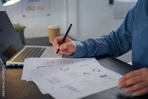 Man analyzing graph paper while sitting by desk at office 
