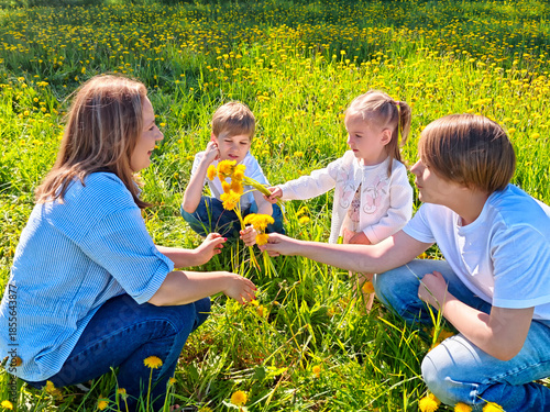 Children enjoying a sunny day picking flowers with their mother in a vibrant green field filled with dandelions